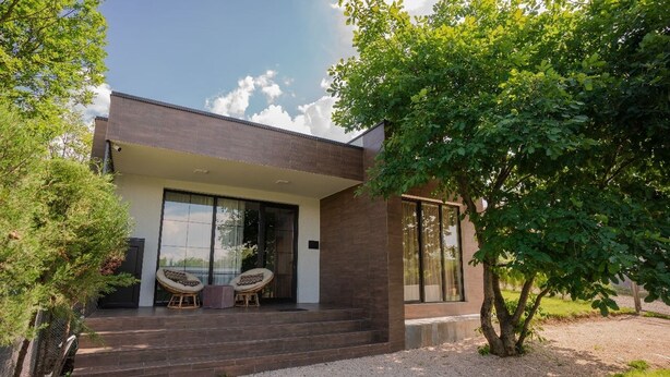 A modern house with a covered porch, large windows, and a tree in the foreground. - Villa Ipanema (Telavi)