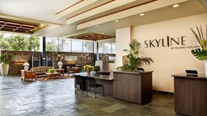 A reception area with a stone wall, wooden reception desk, and seating area with a sofa and chairs. - Glam Condo Located in Central Waikiki, Panoramic Ocean View, & Full Kitchen!
 (Honolulu)