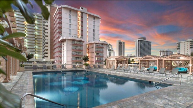 A swimming pool with lounge chairs and a view of high-rise buildings. - Glam Condo Located in Central Waikiki, Panoramic Ocean View, & Full Kitchen!
 (Honolulu)
