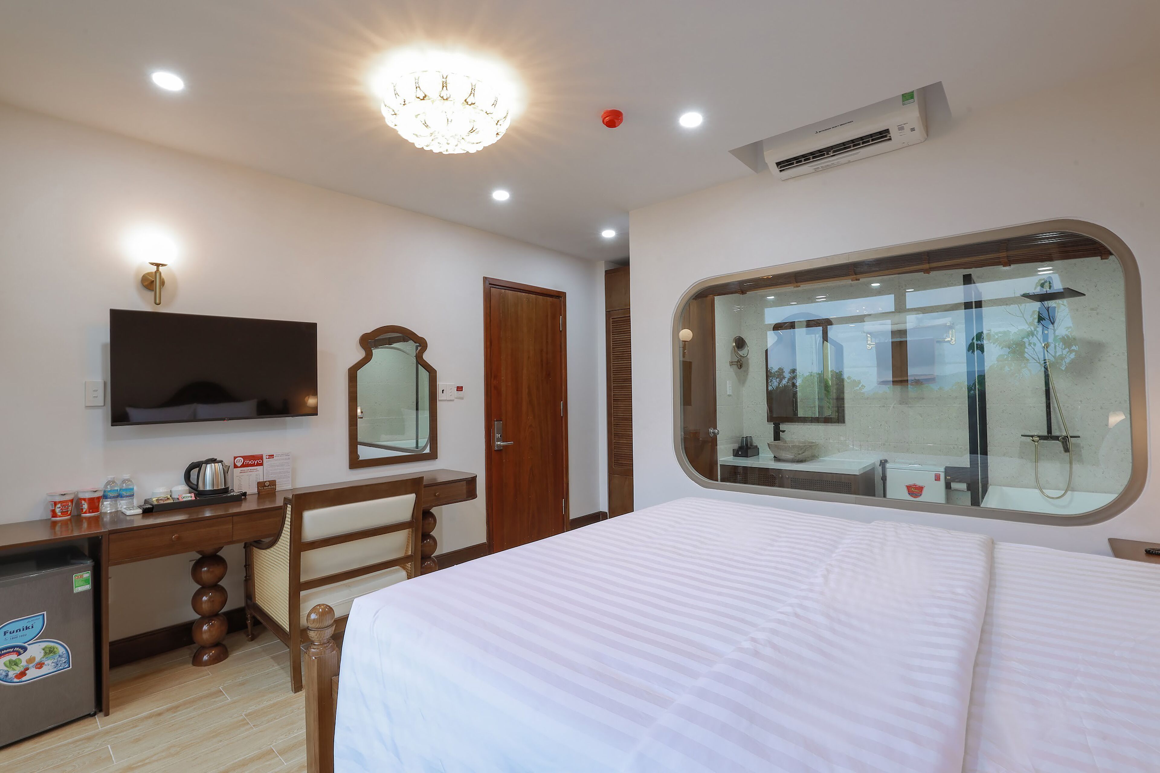 Habitación de hotel con cama, escritorio con silla, espejo, minibar y ventana con vistas al exterior.
