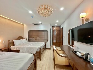 Habitación de hotel con dos camas, un televisor, un escritorio con hervidor y un candelabro.