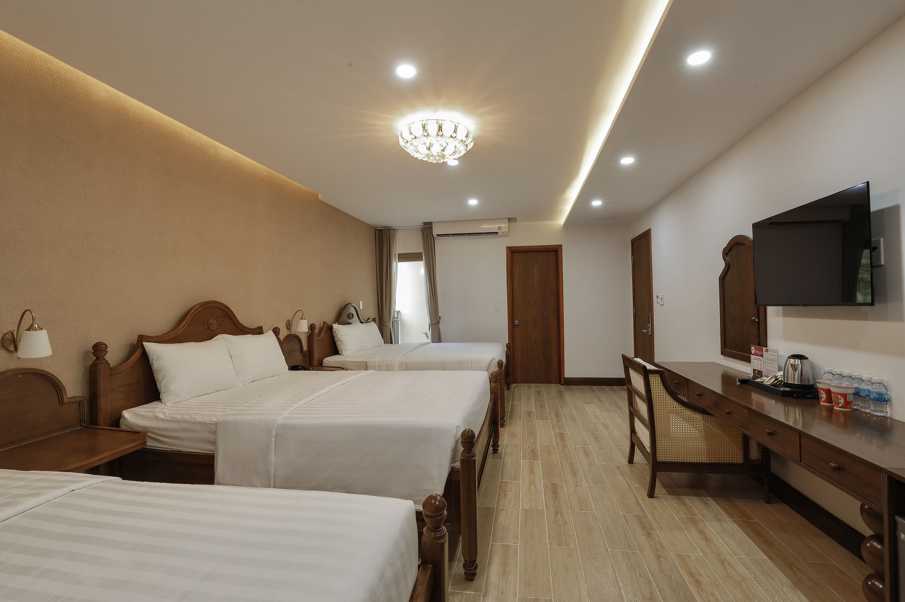A hotel room with three beds, a desk with a television, and a chandelier.