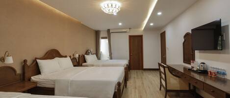 A hotel room with three beds, a desk with a television, and a chandelier.
