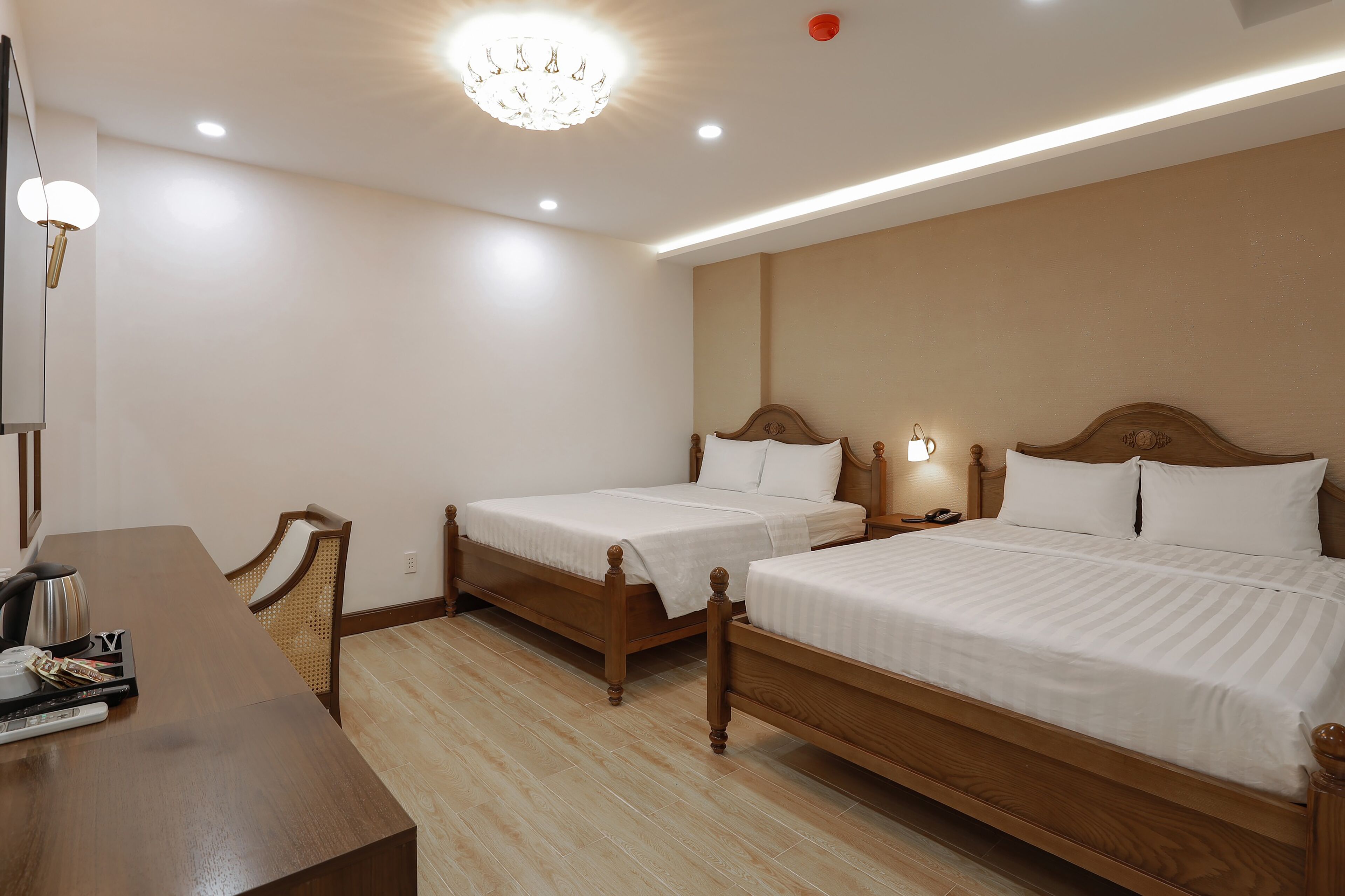 A hotel room with two wooden beds, a wooden desk, and a chandelier.