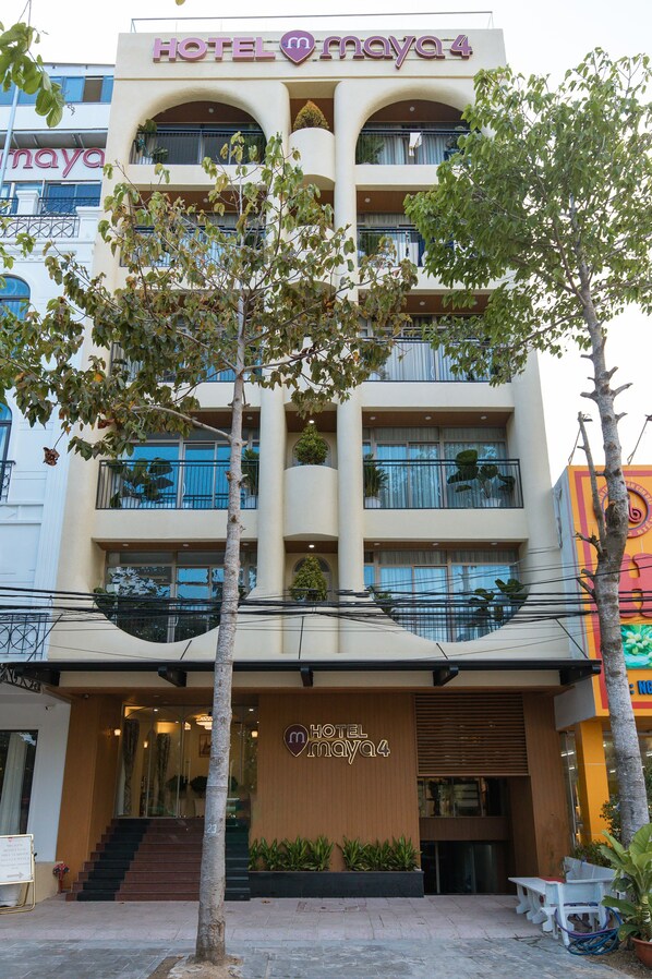 Un hotel de varios pisos con balcones, una escalera que conduce a la entrada y asientos al aire libre.