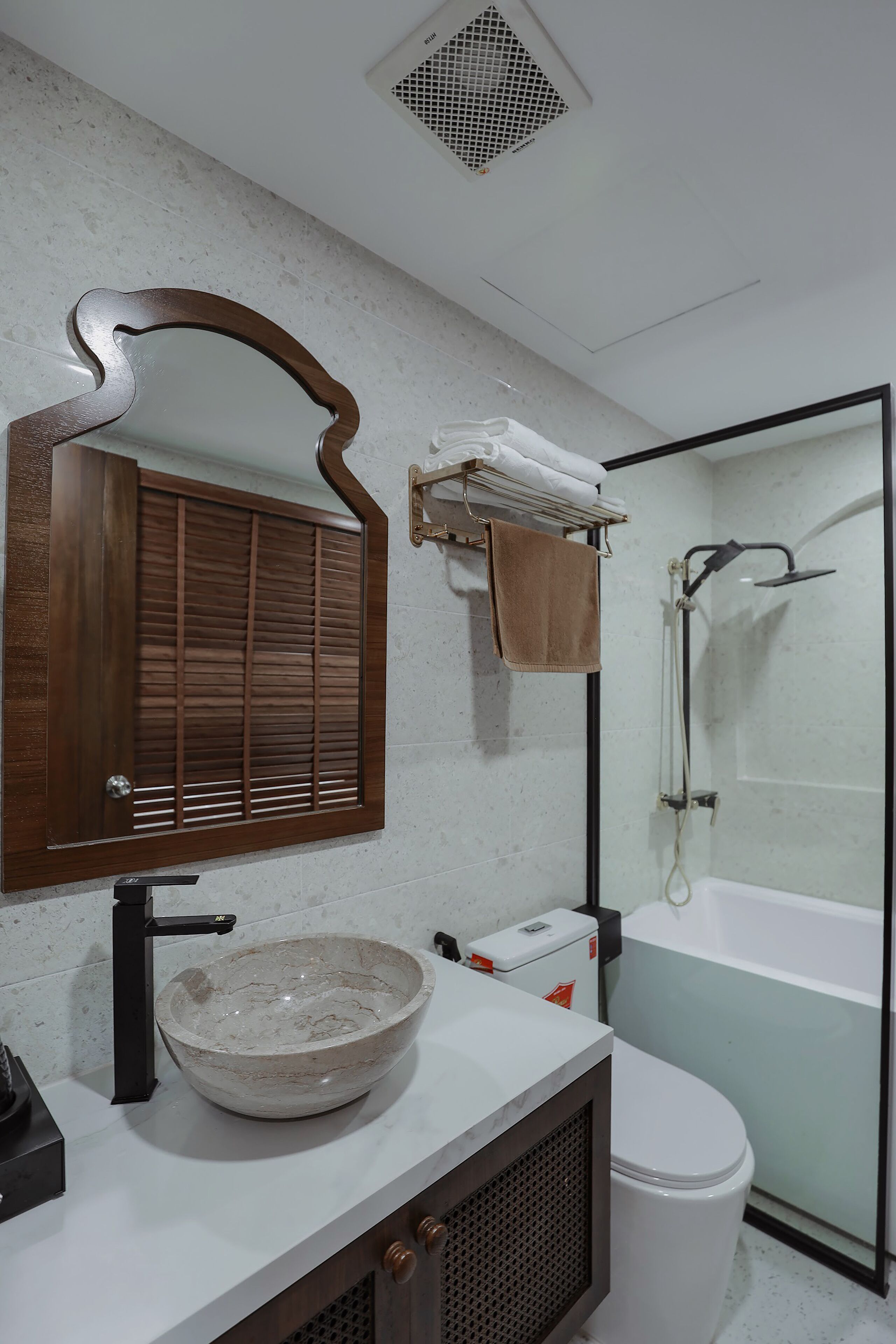 A bathroom with a marble sink, a wooden-framed mirror, a towel rack with a towel, a toilet, and a glass-enclosed shower.