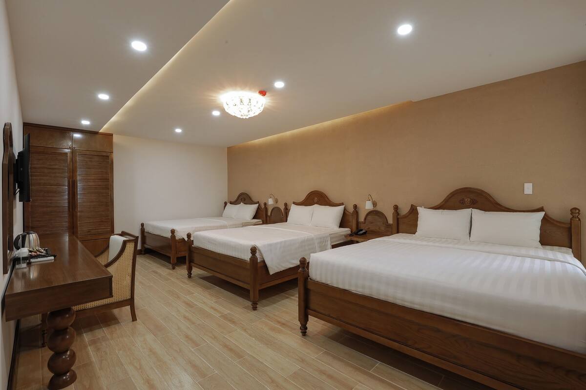 A hotel room with three wooden beds, a wooden desk, and a television.