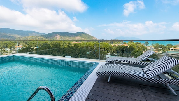 A pool with lounge chairs, a wooden deck, and a view of mountains and greenery.
