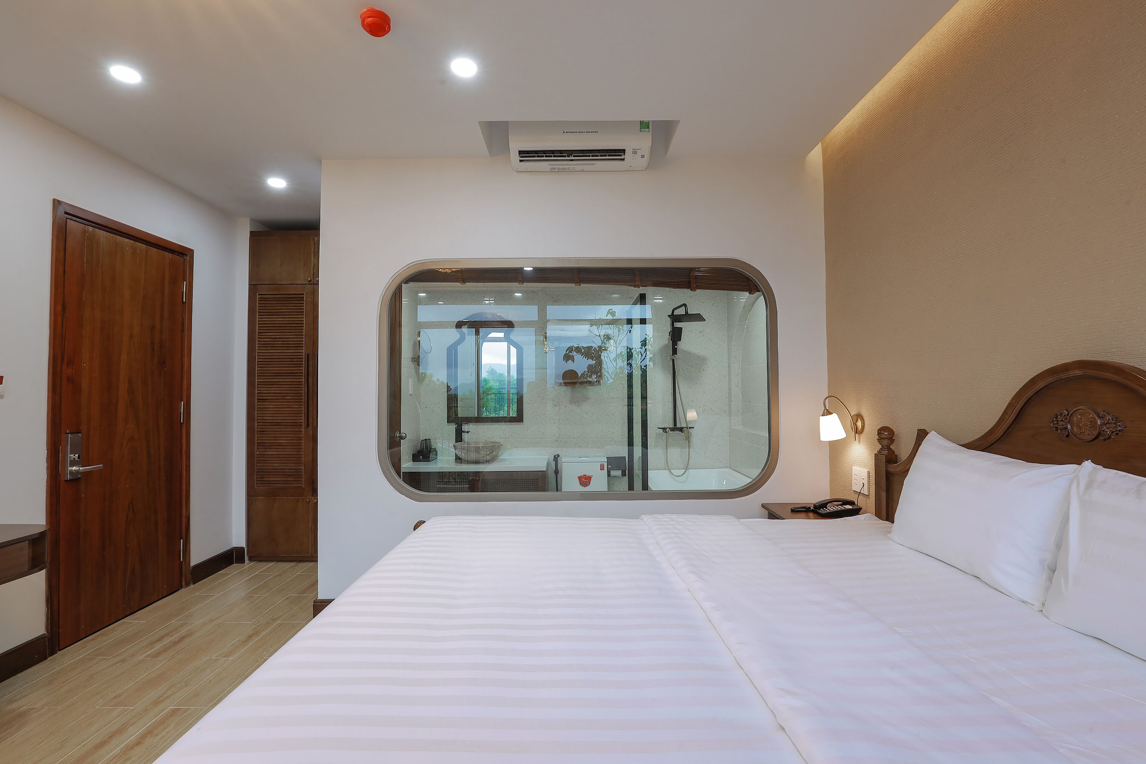 Une chambre d’hôtel dotée d’un grand lit, d’une armoire en bois, d’une salle de bain avec une douche à parois de verre et d’une fenêtre donnant sur l’extérieur.