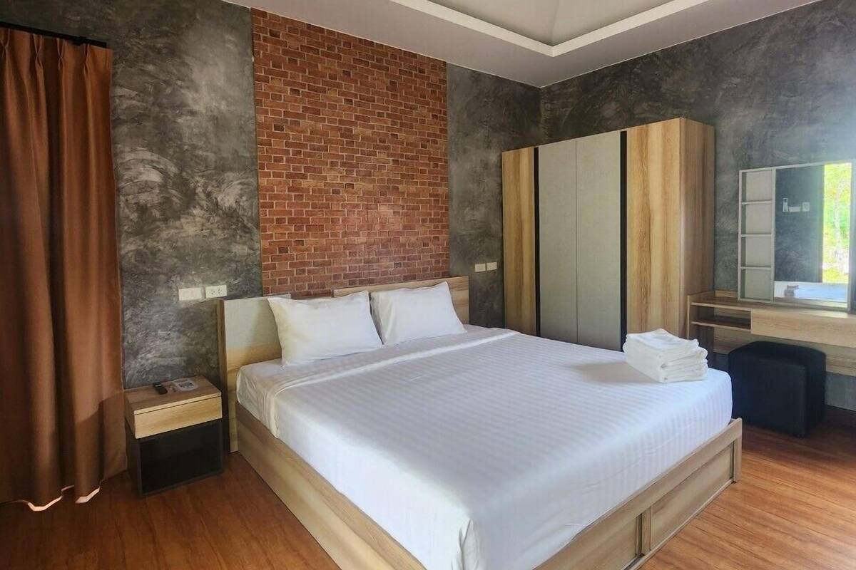 A modern bedroom with a large bed, wooden flooring, a brick accent wall, and a desk with a mirror.