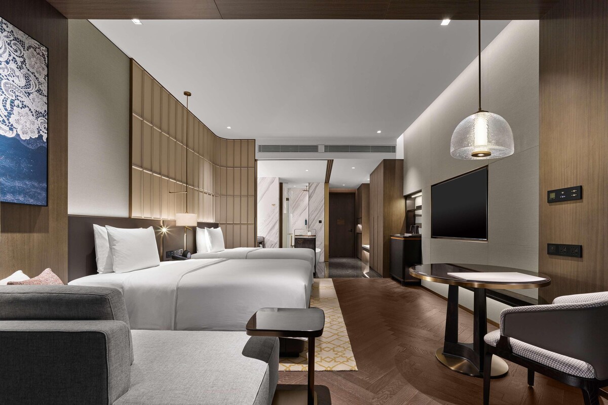 A modern hotel room with a large bed, a TV, a desk, and a seating area.