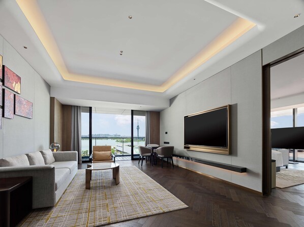 A modern living room with a large flat-screen TV, a sofa, a coffee table, and a view of a cityscape through large windows. - Hilton Changshu (Suzhou)