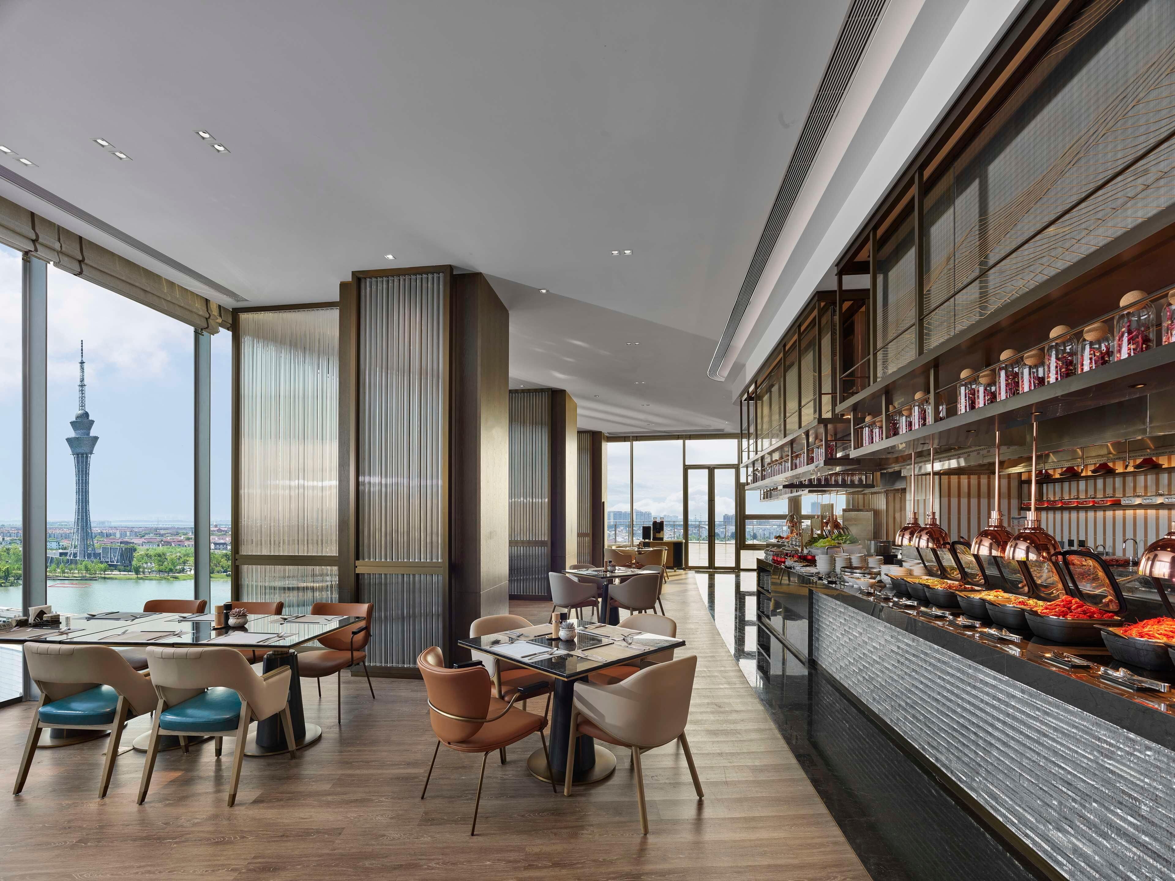 Een modern restaurant met een hoge plafond, grote ramen en een buffetgedeelte.