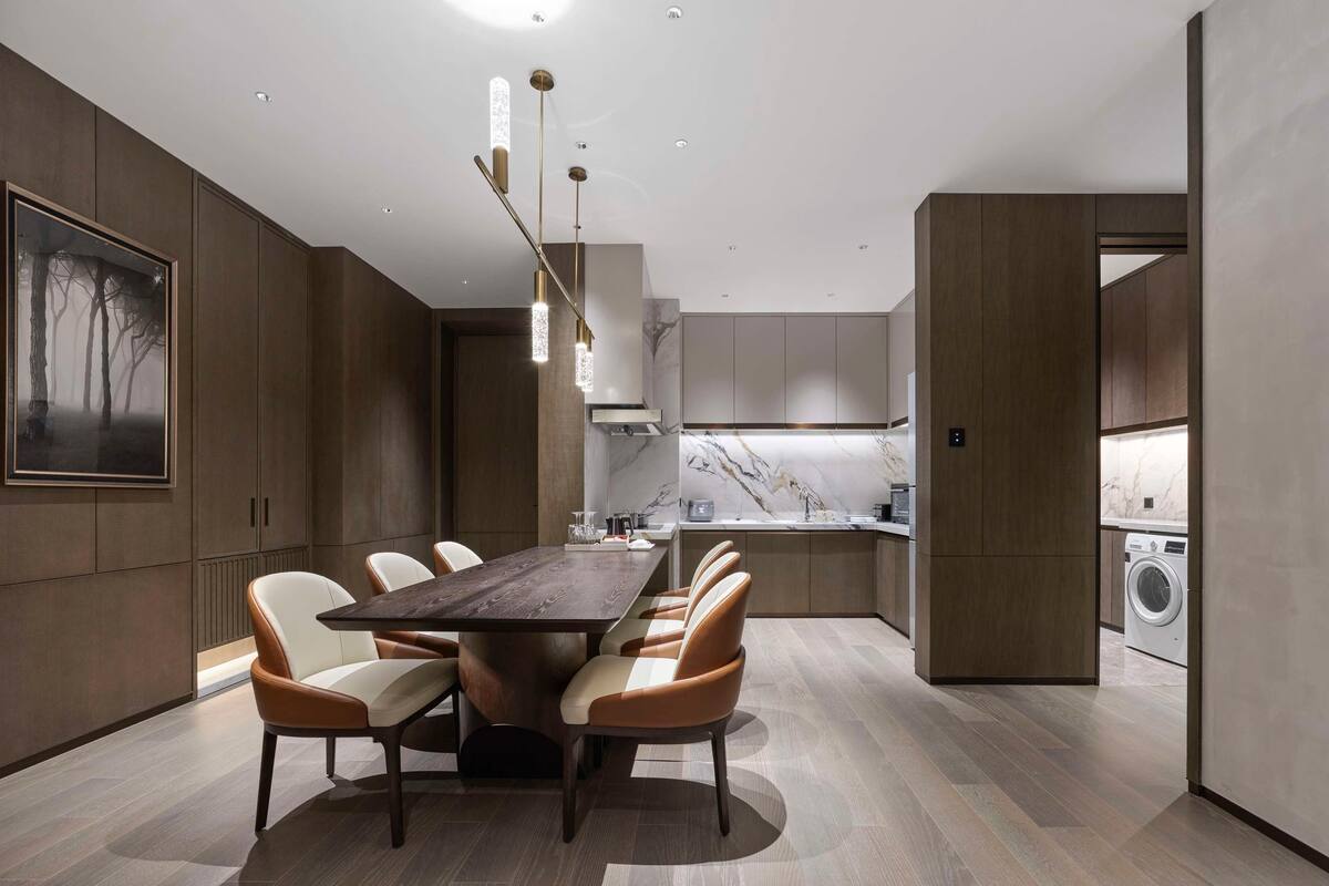 A modern kitchen with a marble backsplash, a dining area with a wooden table and chairs, and a large framed artwork on the wall.