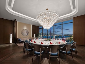 A modern dining room with a round table set for six, large windows offering a city view, and a prominent chandelier. - Hilton Changshu (Suzhou)