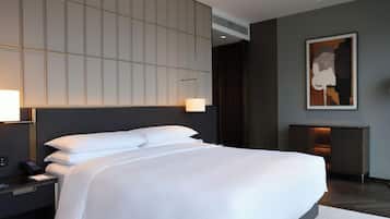 A modern hotel room with a large bed, a bedside table with a lamp, a wall-mounted air conditioner, and a framed artwork above the bed.