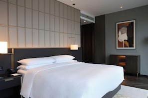 A modern hotel room with a large bed, a bedside table with a lamp, a wall-mounted air conditioner, and a framed artwork above the bed. - Hilton Changshu (Suzhou)