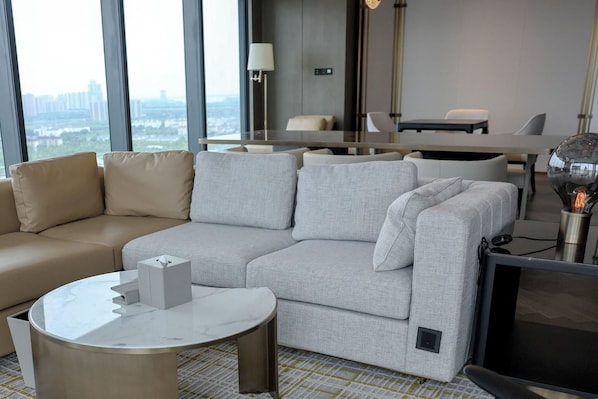 A modern living room with a beige sofa, a grey sectional, a round coffee table, and a flat-screen TV. - Hilton Changshu (Suzhou)