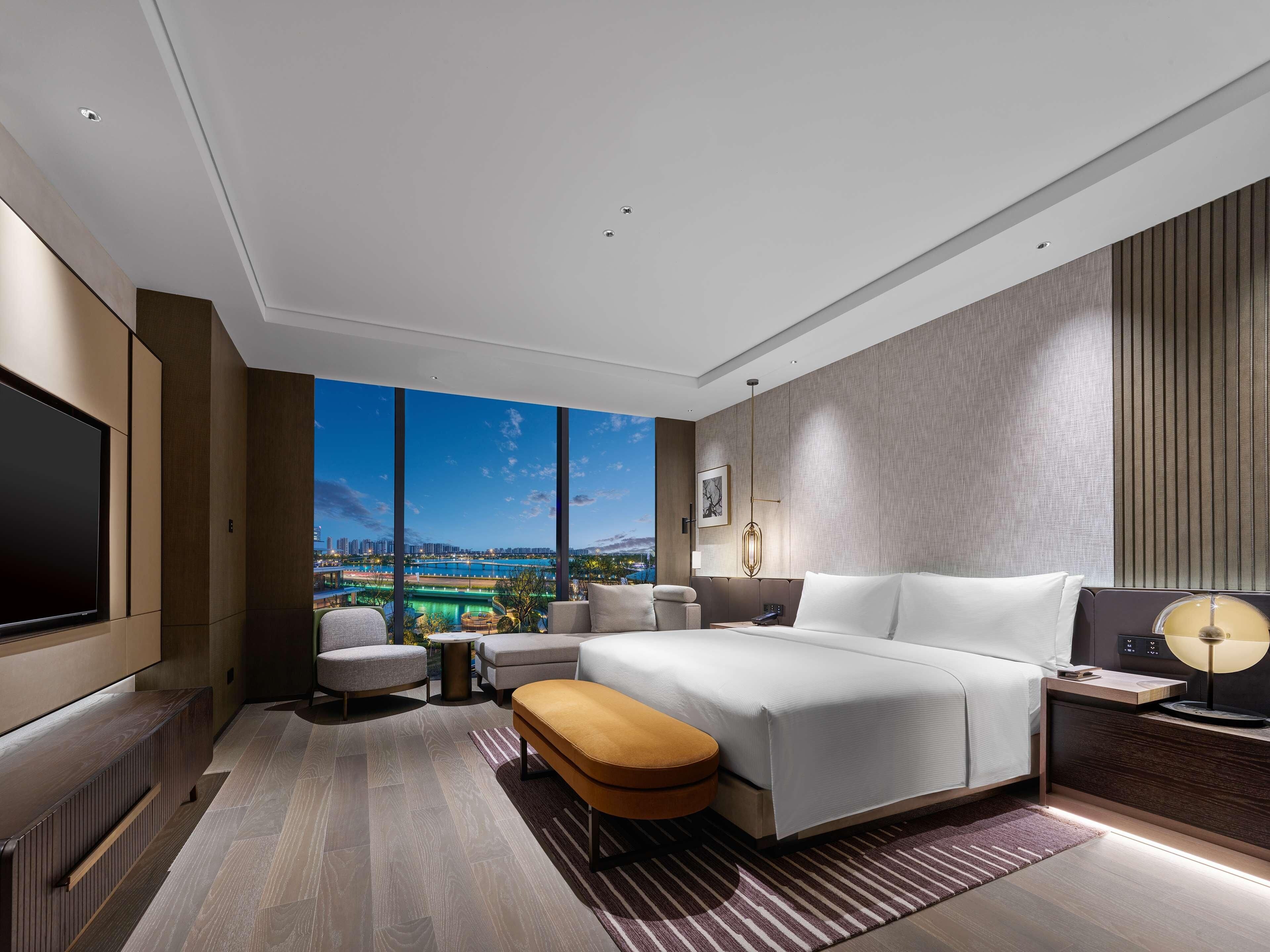Een moderne hotelkamer met een groot bed, een televisie en uitzicht op een stadsbeeld.