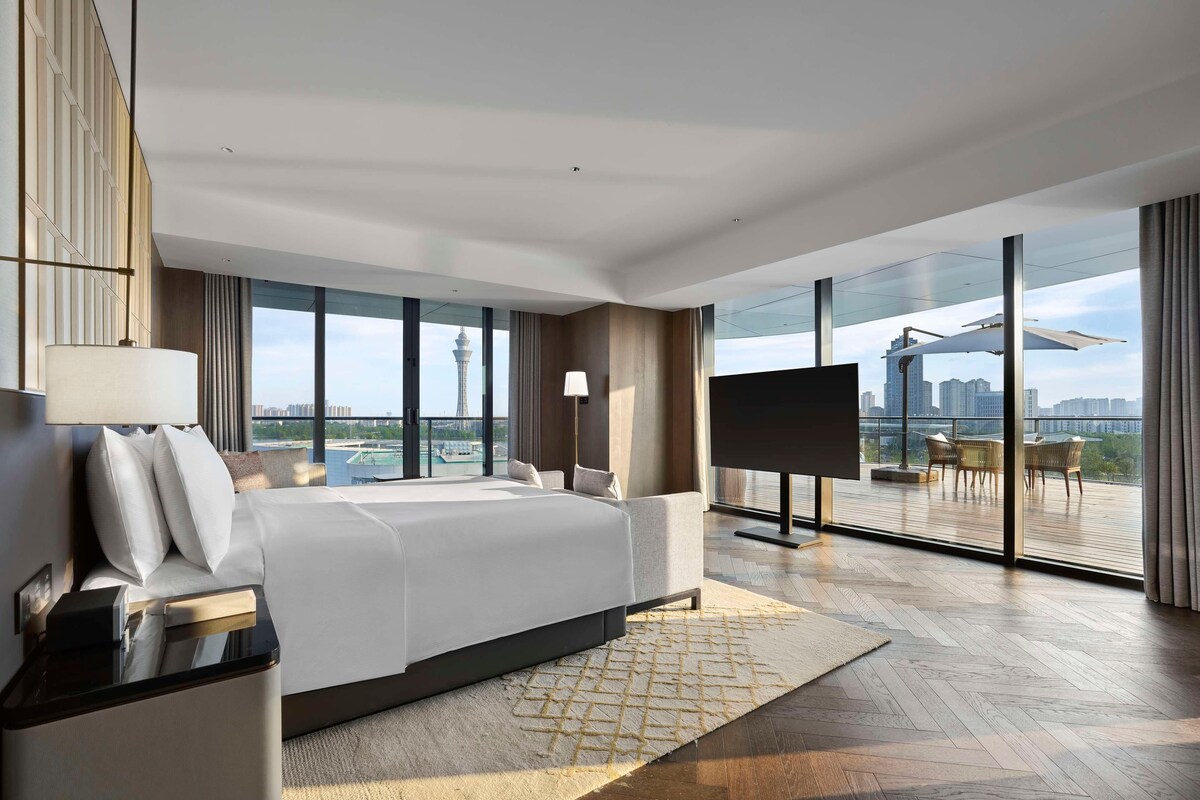 A modern hotel room with a large bed, a TV, and a balcony with a city view.