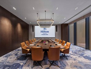 A conference room with a long table, multiple chairs, a large screen displaying 'Hilton CHANGSHU', and a modern chandelier. - Hilton Changshu (Suzhou)