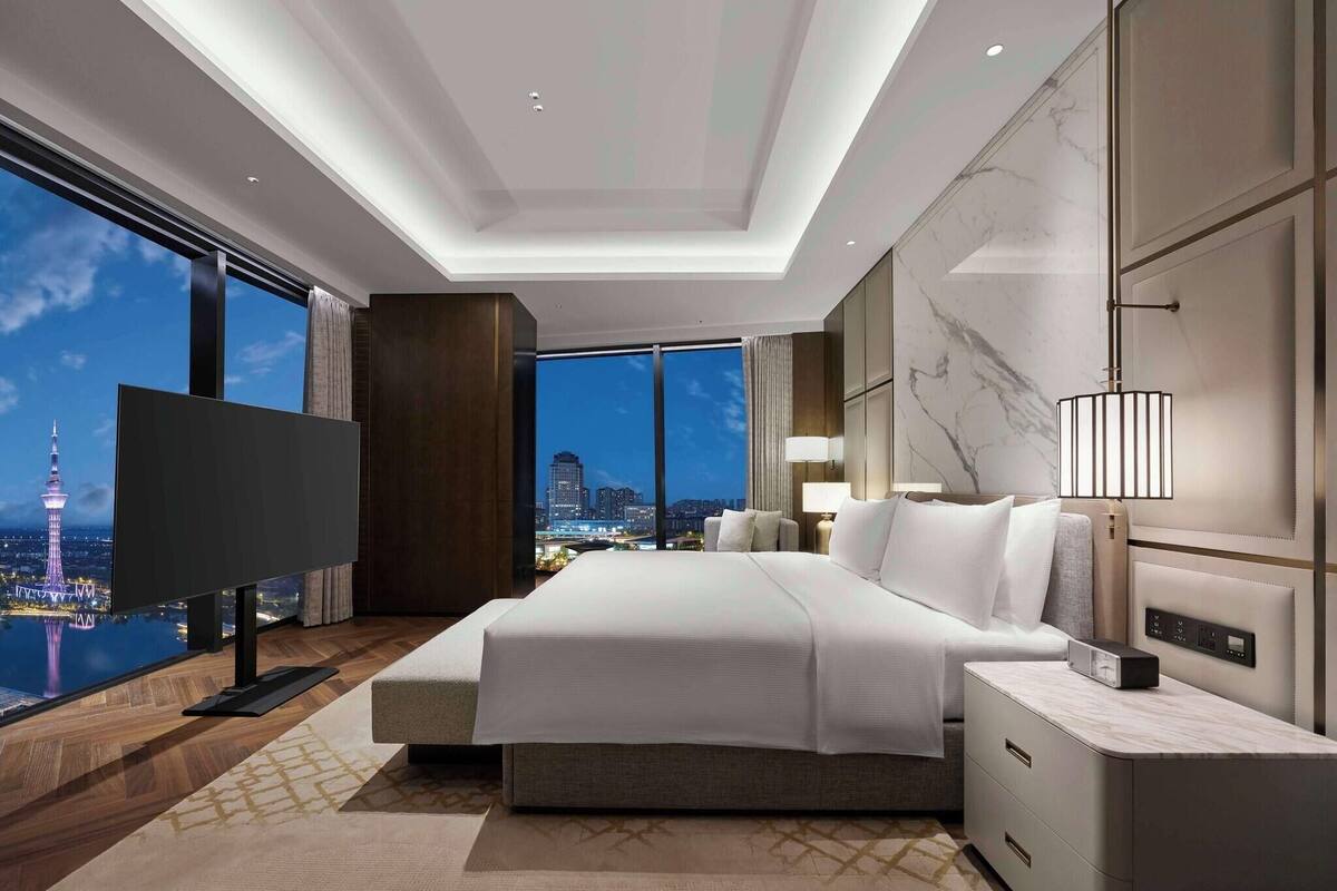 A modern hotel room with a large bed, a TV, and a city view.