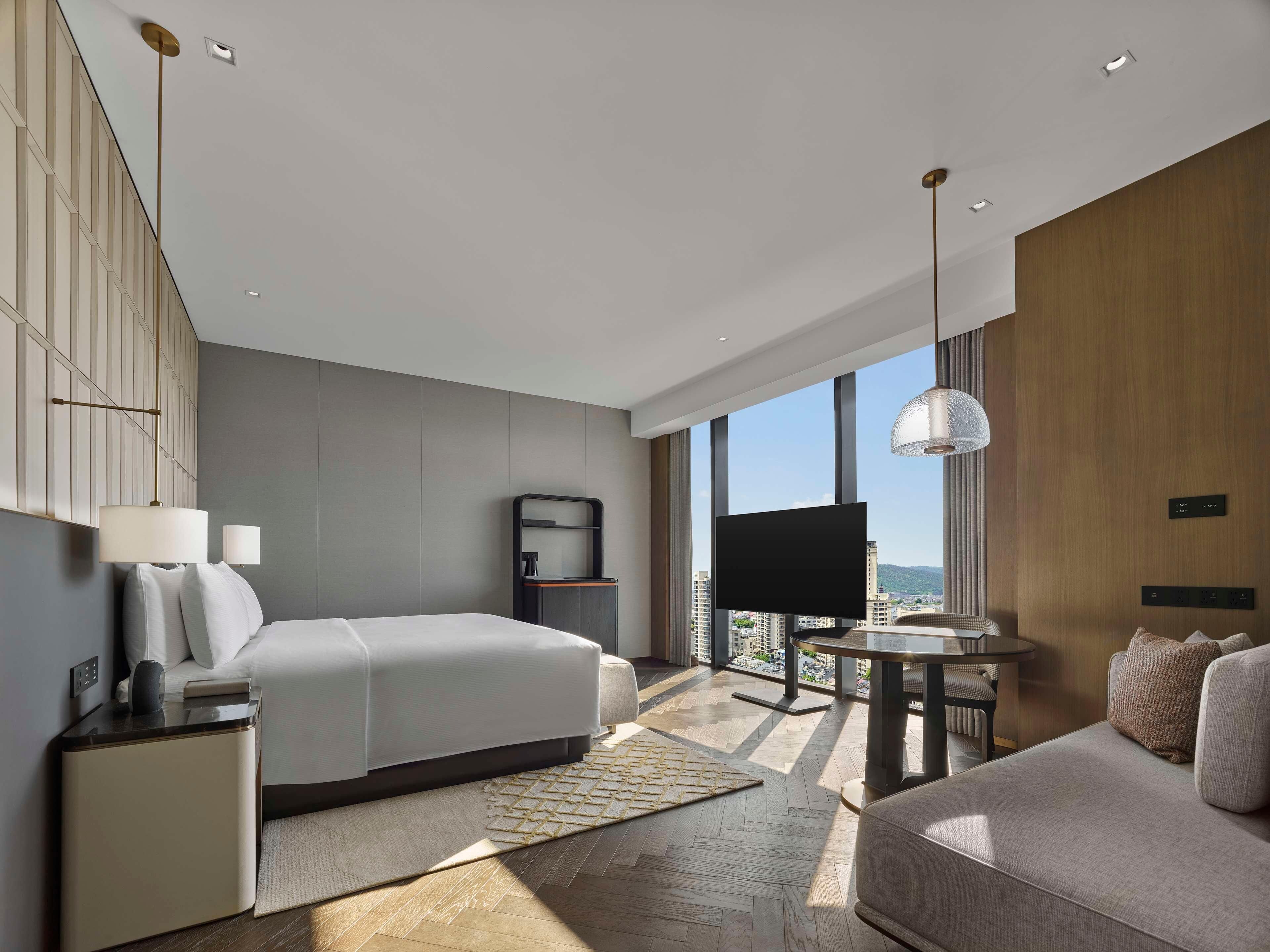 A modern hotel room with a bed, a sofa, a desk, and a TV.