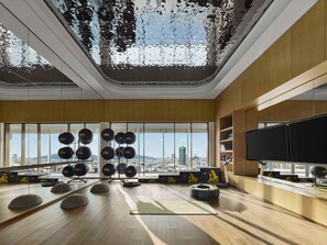 Ett rymligt gym med träningsutrustning, stora fönster och utsikt över staden.