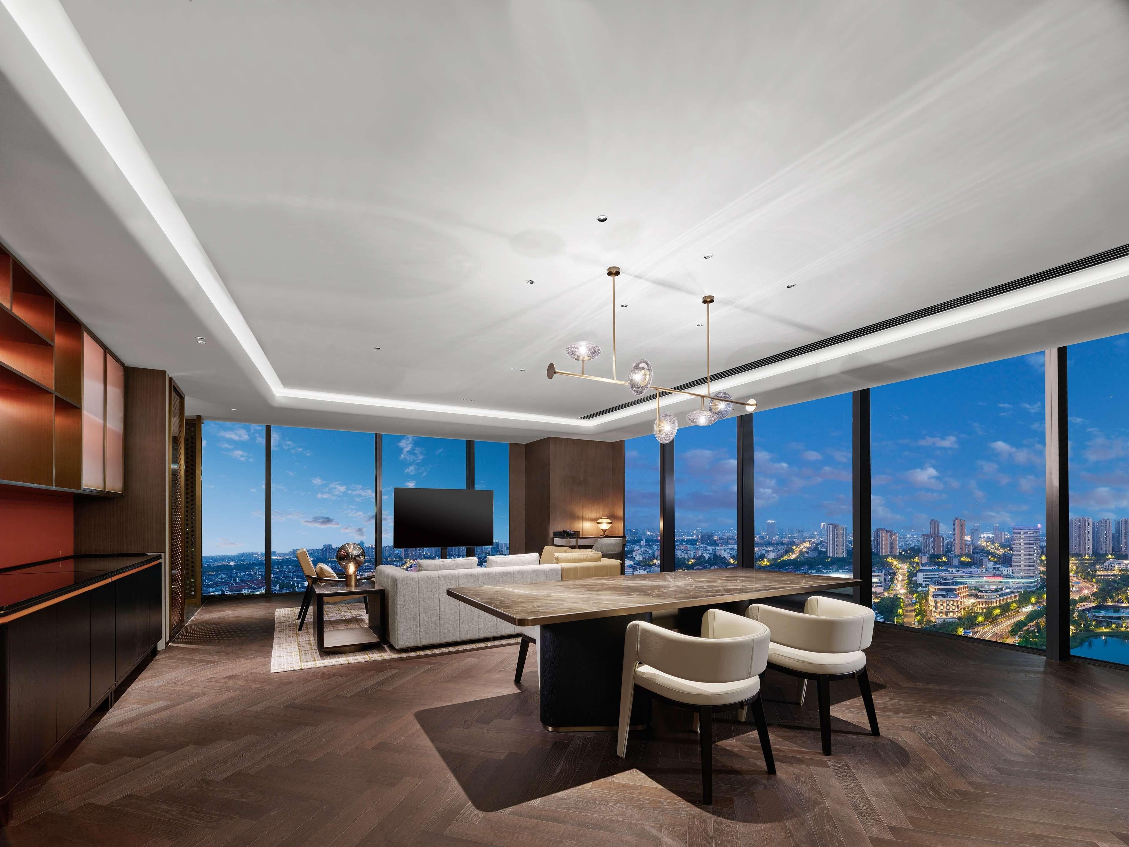A modern living room with a large city view, a flat-screen TV, and a dining area with a wooden table and chairs.