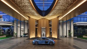 A modern hotel entrance with a blue sports car parked in front, a glass facade, and a ceiling with a light pattern. - Hilton Changshu (Suzhou)