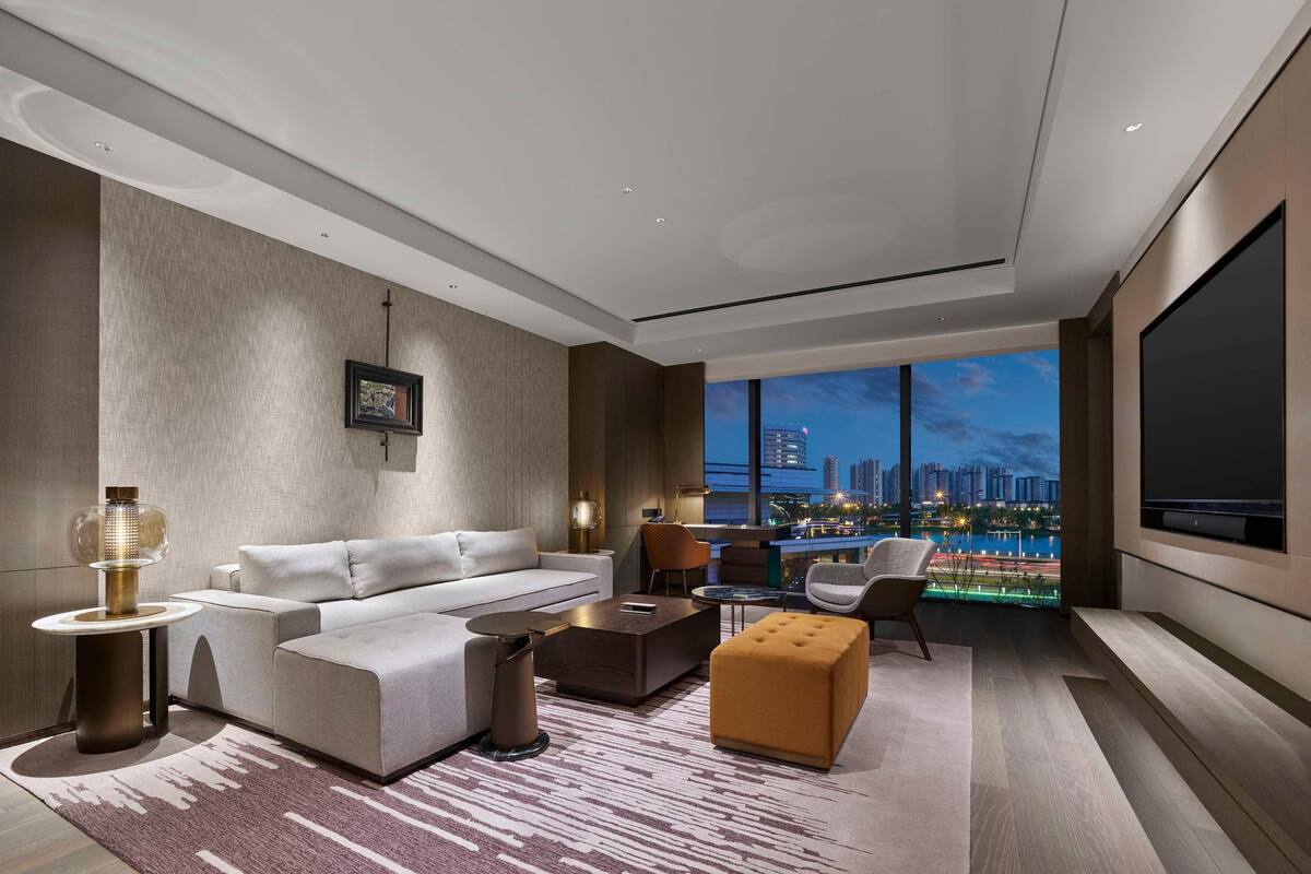 A modern living room with a large window, a sofa, a coffee table, and a TV.