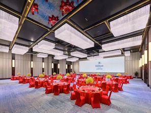 A large conference room with round tables, red chairs, and a Hilton branding screen. - Hilton Changshu (Suzhou)