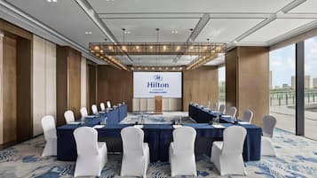 A conference room with a large screen displaying the Hilton logo, white chairs, and a blue carpet.