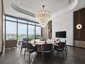 A modern dining room with a large chandelier, a round table set for six, and a city view through large windows. - Hilton Changshu (Suzhou)