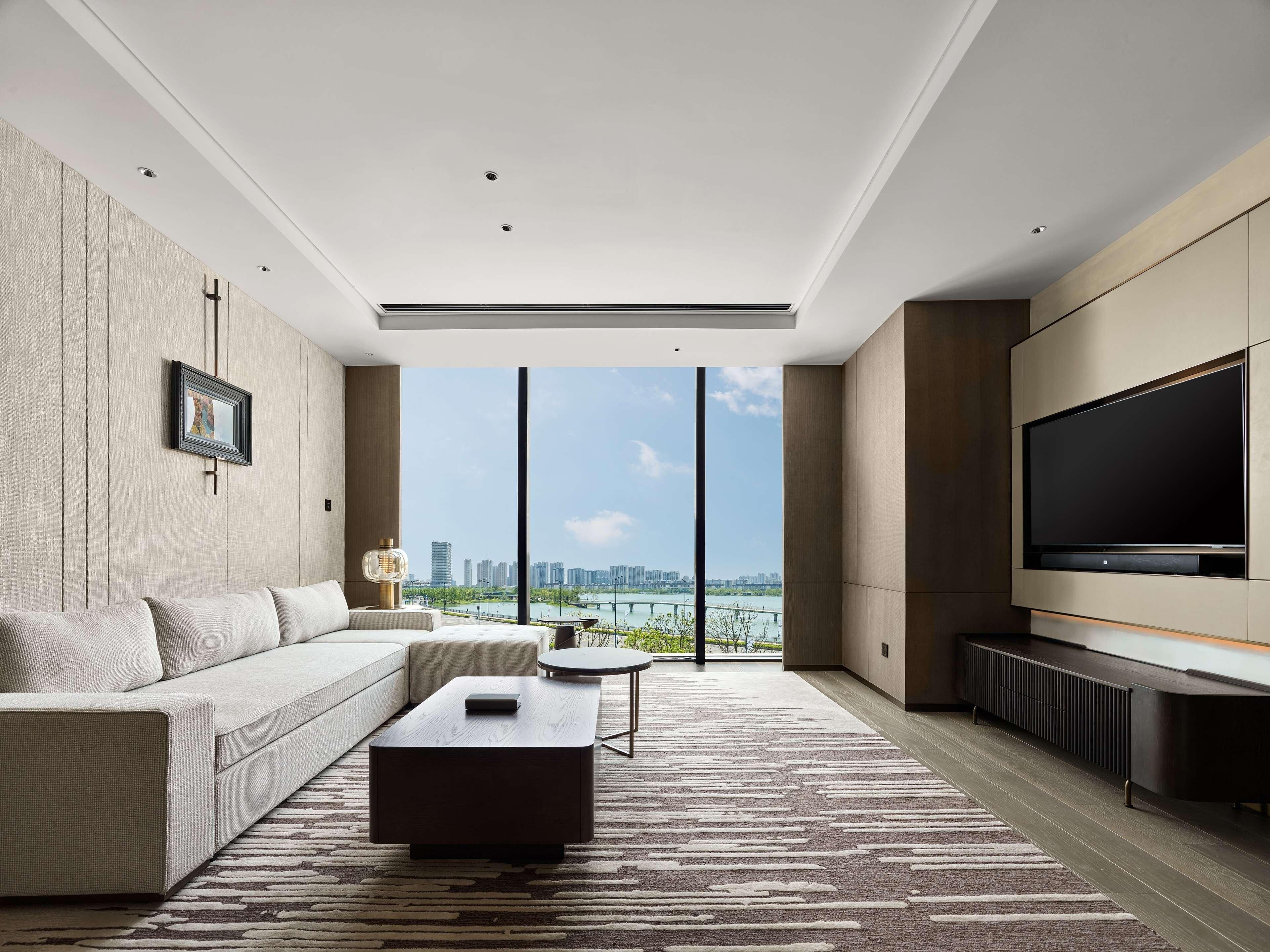 A modern living room with a large TV, a sofa, a coffee table, and a view of a cityscape.