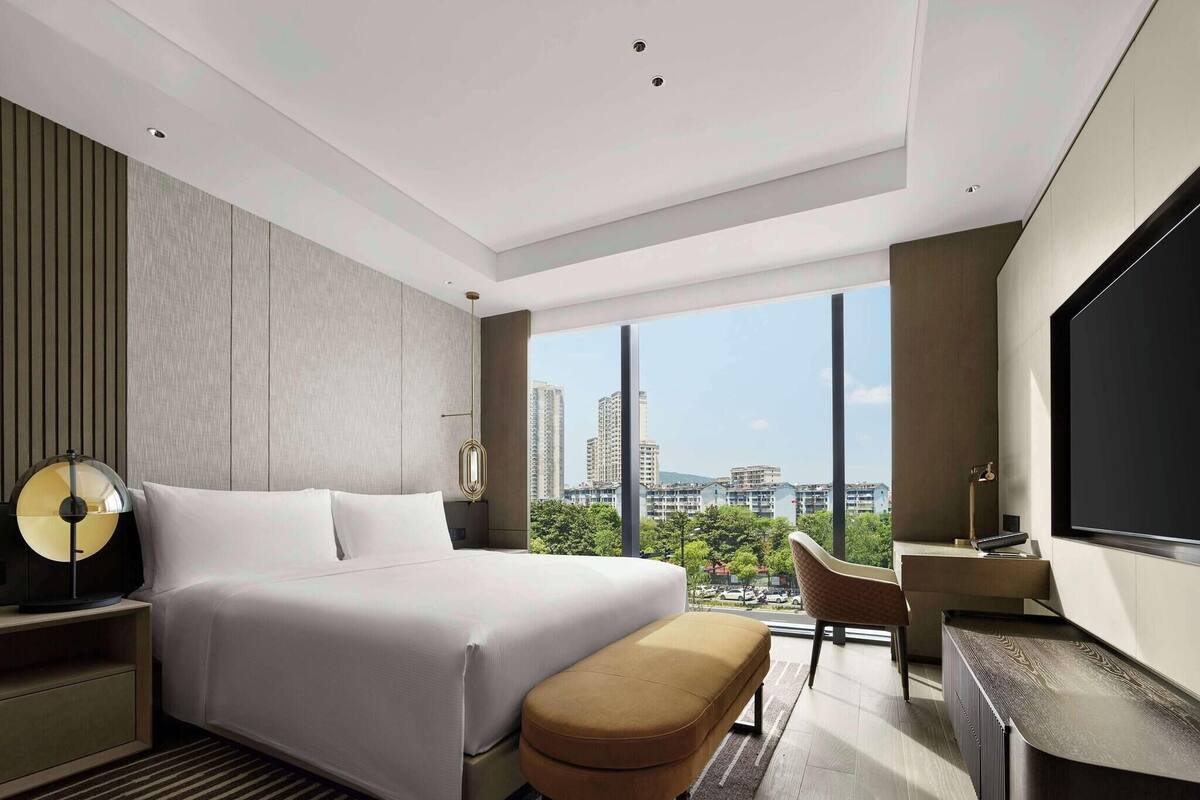 A modern hotel room with a large bed, a desk, a chair, and a TV.