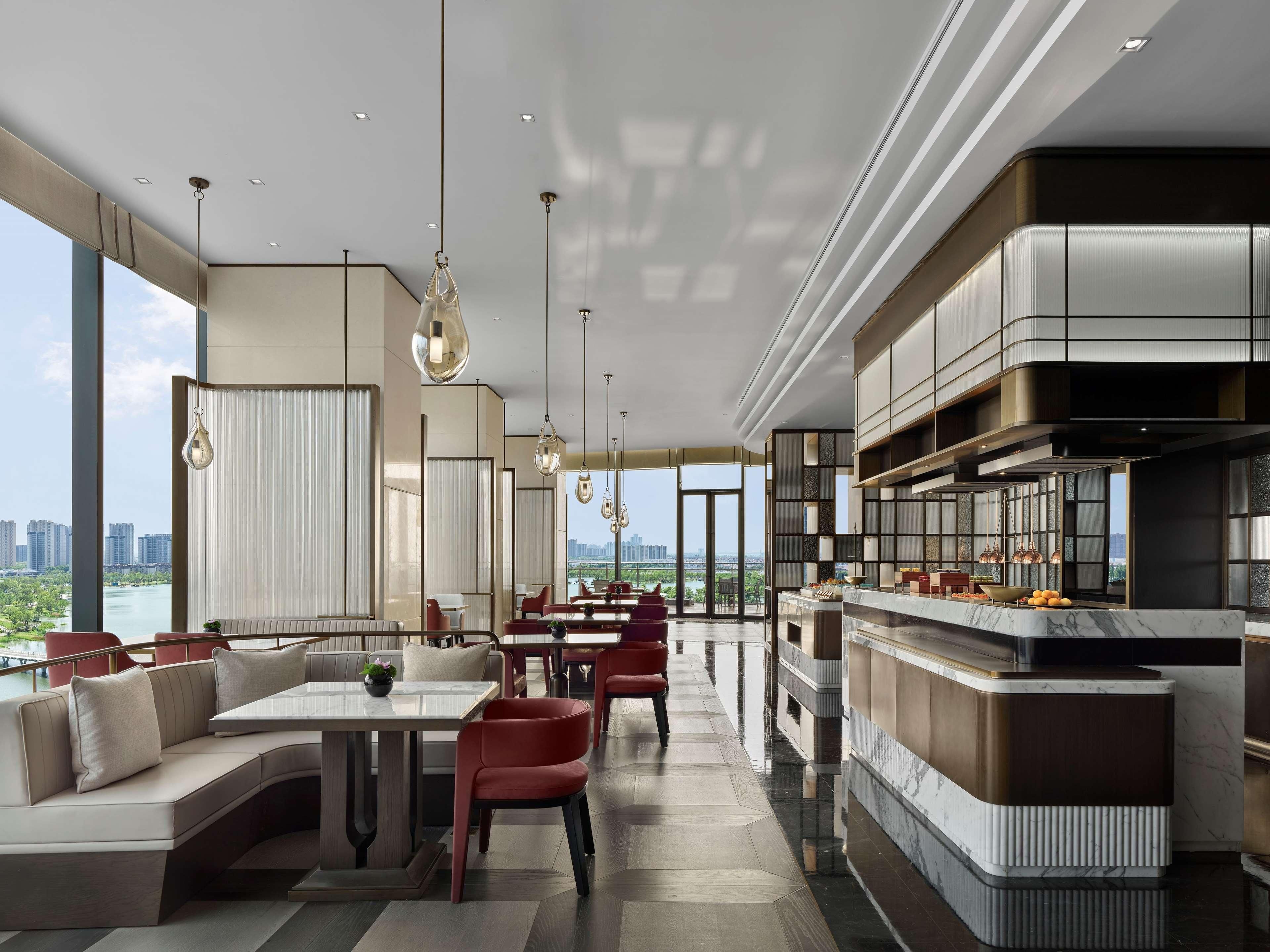 Un restaurante moderno con una barra larga, zona de asientos y amplios ventanales que ofrecen vista a la ciudad.