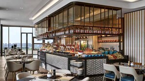 A modern restaurant with a central bar area, multiple dining tables, and a city view. - Hilton Changshu (Suzhou)
