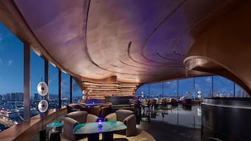 A modern lounge with a curved ceiling, a bar area, and a seating arrangement with a view of the cityscape.