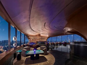 Een moderne lounge met een gebogen plafond, een bar en een zithoek met uitzicht op de stad.