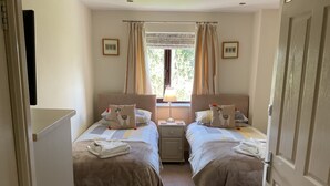 Une chambre d’hôtel avec deux lits, une fenêtre avec des rideaux, une table de chevet avec une lampe et une porte.