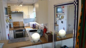 Een compacte keuken met witte kastjes, een broodrooster, een waterkoker en een magnetron. Een grote spiegel weerspiegelt de keuken en er staat een brandblusser op het aanrecht.