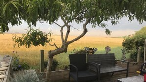 Een houten terras met een bankje en een tafel, met uitzicht op een veld.