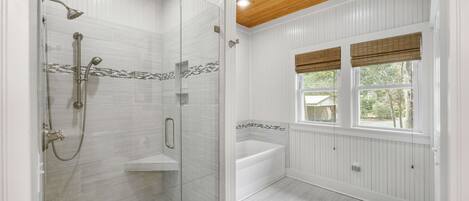 A bathroom with a glass-enclosed shower, a bathtub, and a window with blinds.