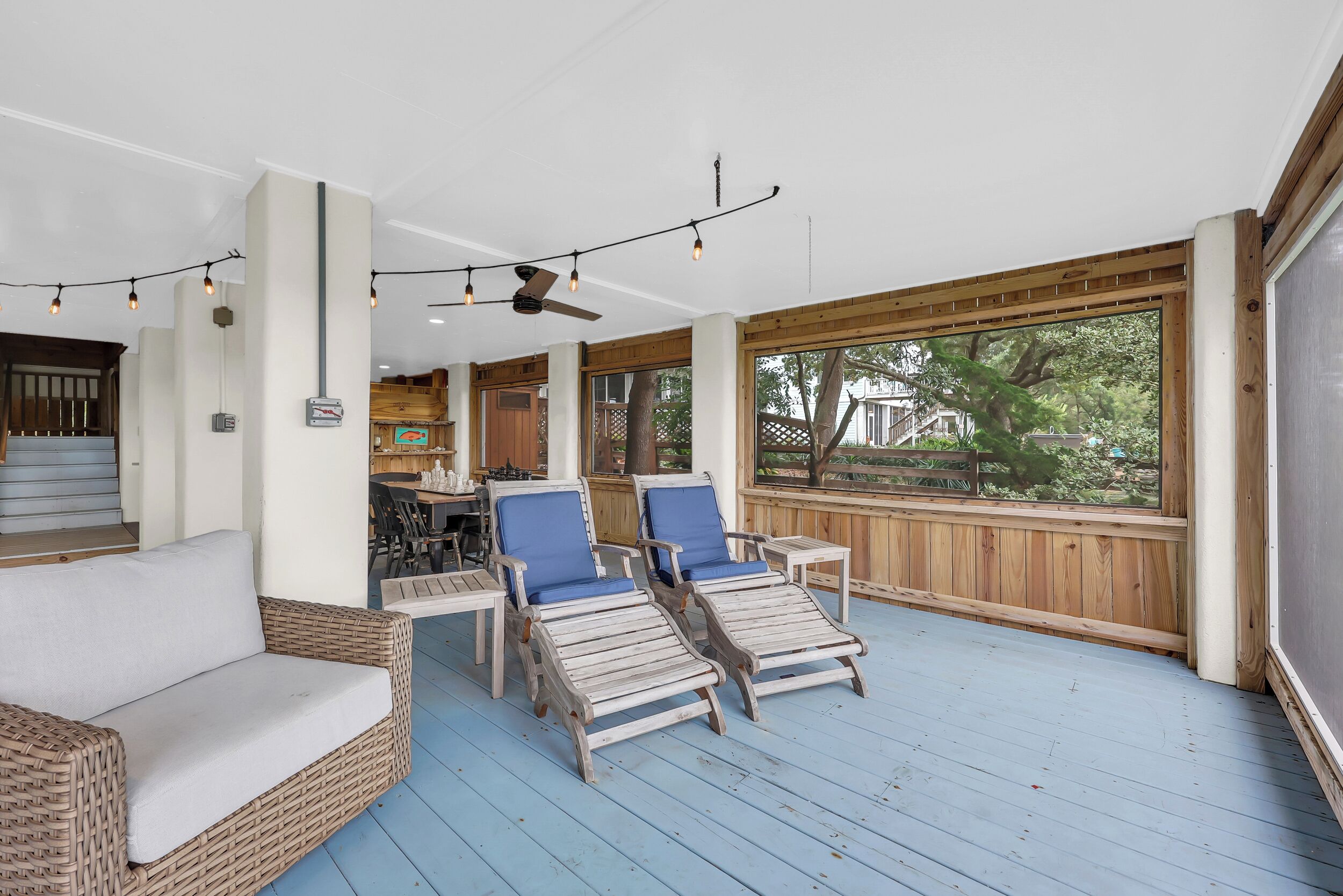 A covered outdoor seating area with wicker furniture, wooden deck flooring, and string lights.