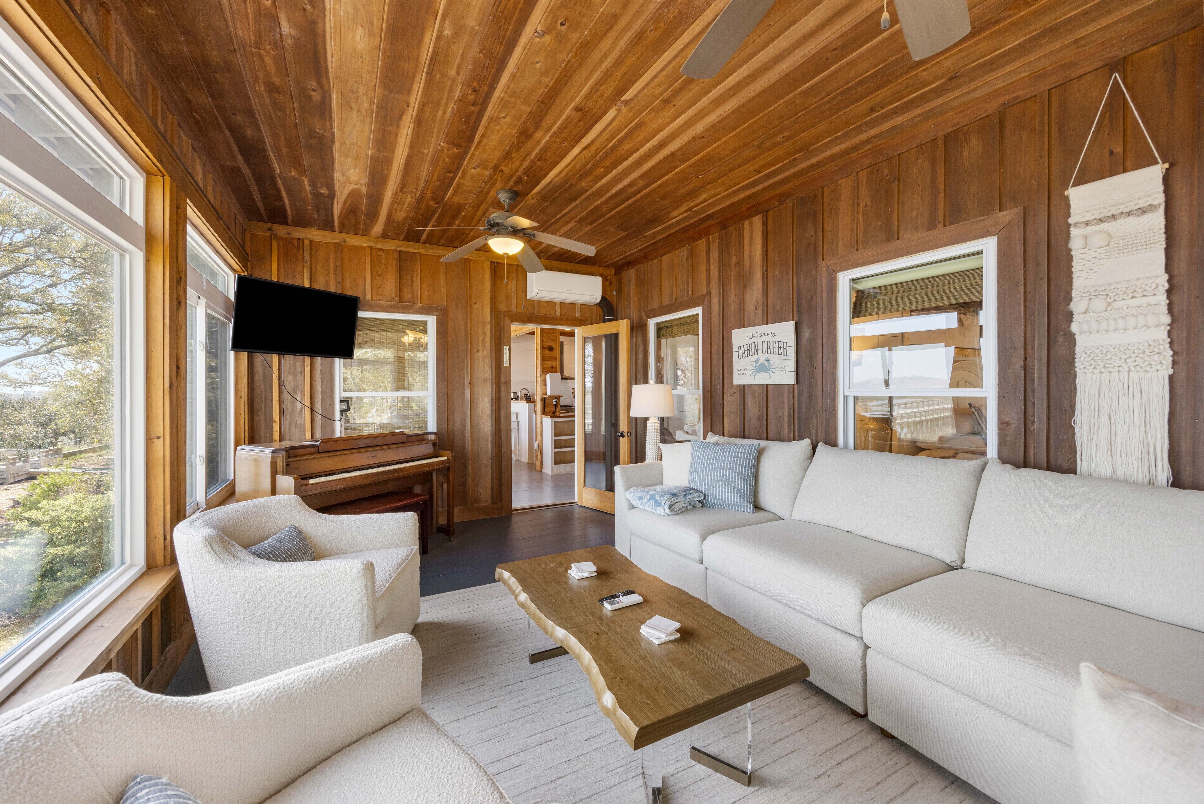 Een kamer in een hut met houten plafond, een flatscreen televisie, een bank, een bijzettafeltje en uitzicht door de ramen.