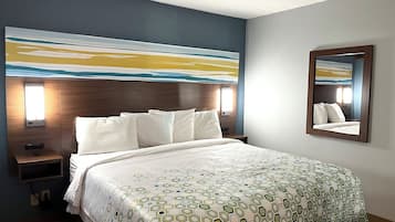 A hotel room with a large bed, a nightstand, a wall-mounted mirror, and a painting above the bed.