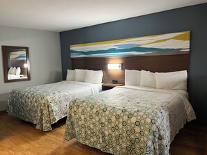 A hotel room with two beds, a nightstand, a wall-mounted lamp, and a framed picture. - HomeTowne Studios by Red Roof Amarillo West (Amarillo)