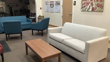 A room with a white sofa, two blue armchairs, and a wooden coffee table. There are posters on the wall and a door with a sign.