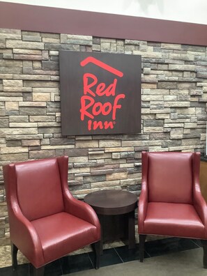 Letrero de Red Roof Inn sobre una pared de piedra, con dos sillones de cuero y una pequeña mesa al frente.